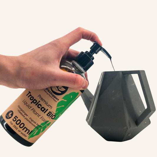 Mano presiona dosificador de alimento líquido bio para plantas tropicales en regadera gris
