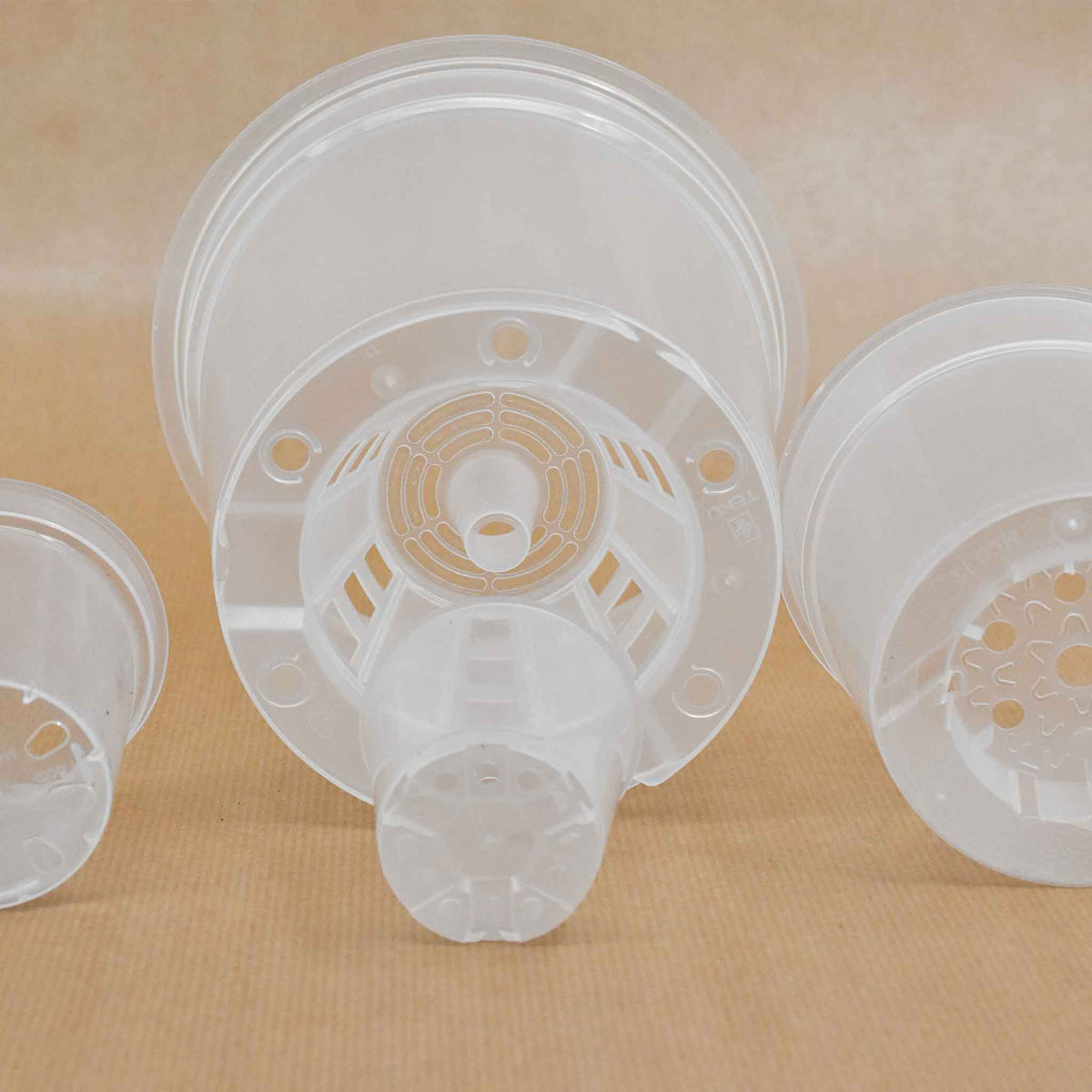 Clear plastic orchid pots stacked, showing slotted drainage bottoms